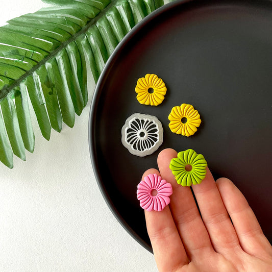 small abstract flower shapes from polymer clay next to a clay cutter on a plate