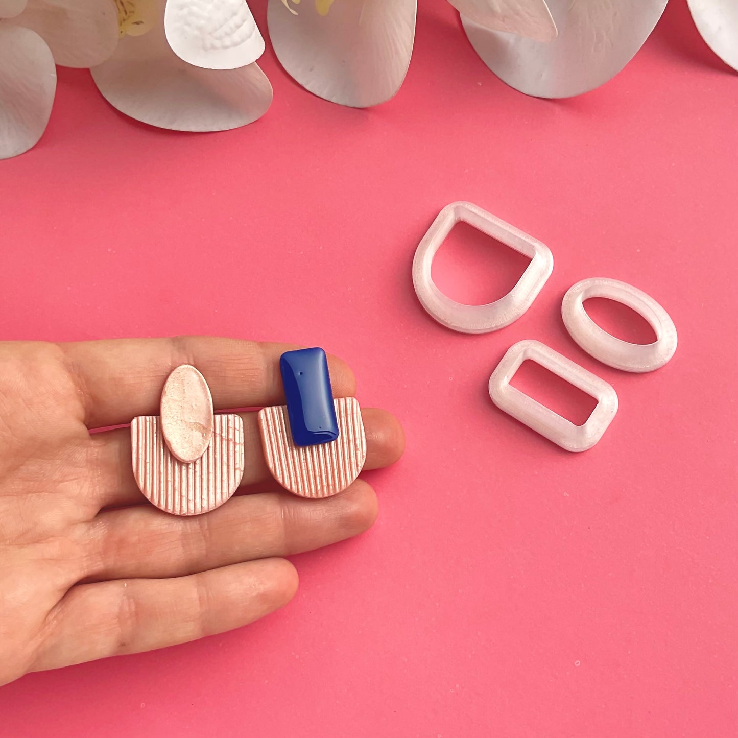 three cutters in different geometric shapes and two polymer clay earrings displayed on a hand