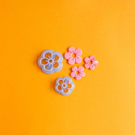 Two daisy shaped cutters of different sizes and three pink polymer clay daisies