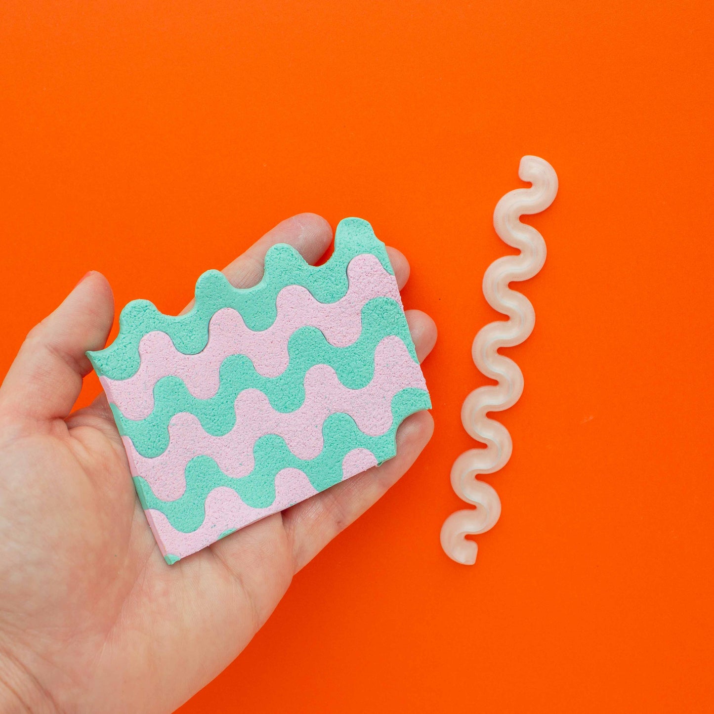 colorful wiggly polymer clay slab in a hand and 1 wiggle blade in an orange background