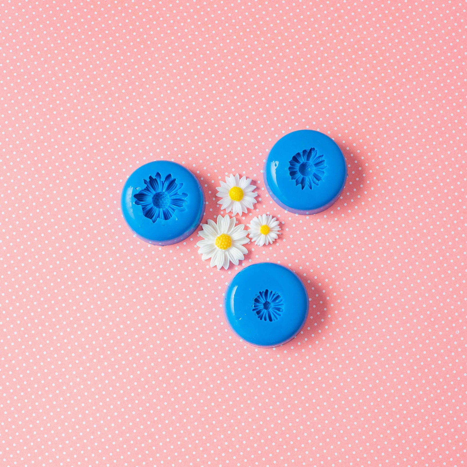 A set of 3 flower silicone molds and three daisies in a pink polka dots background.