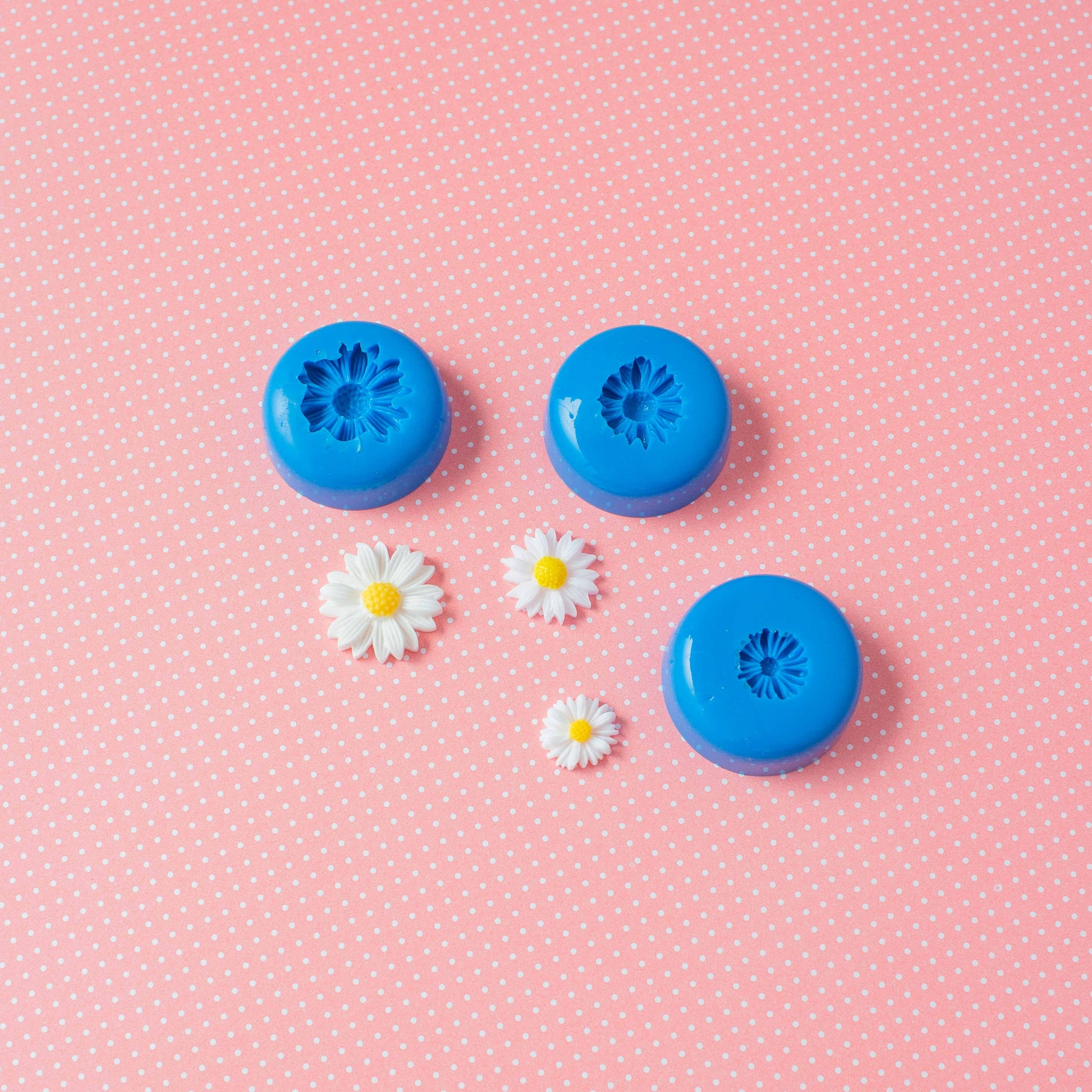A set of 3 flower silicone molds and three daizies in a pink polka dots background.