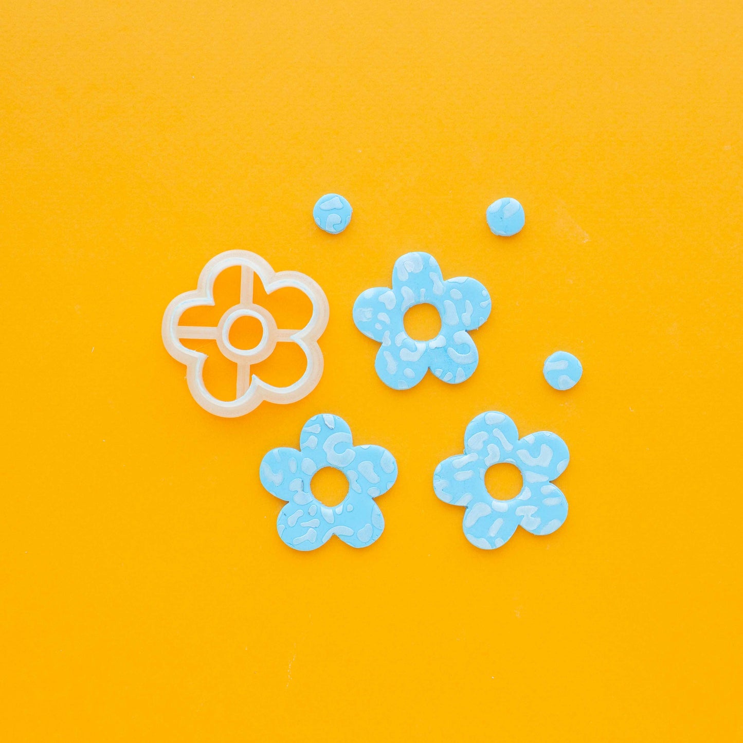 One daisy shaped polymer clay cutter, three flowers and three circles of polymer clay on a yellow background