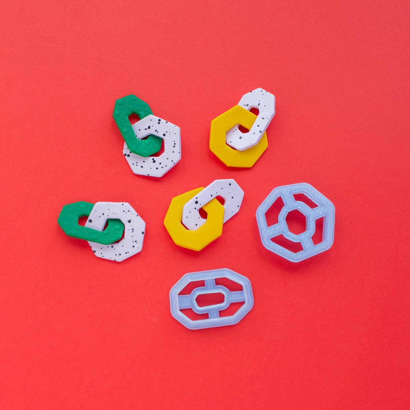 Two organic shaped clay cutters, one oval and one square, and two pairs of link earring on a red background