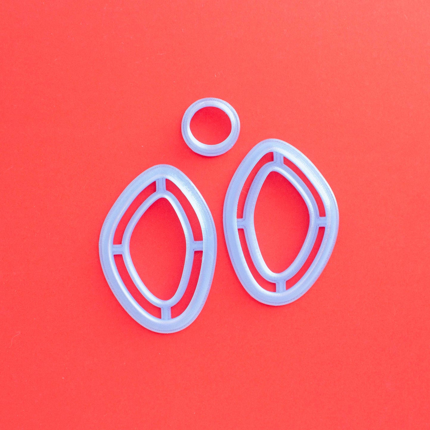 A set of two mirrored organic oval cutters and a stud on a red background. 