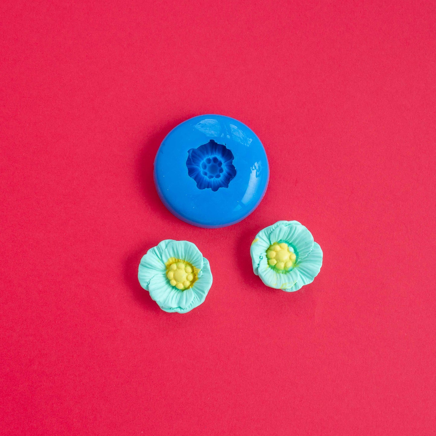 2 clay flowers and siliscone mold on a red background.