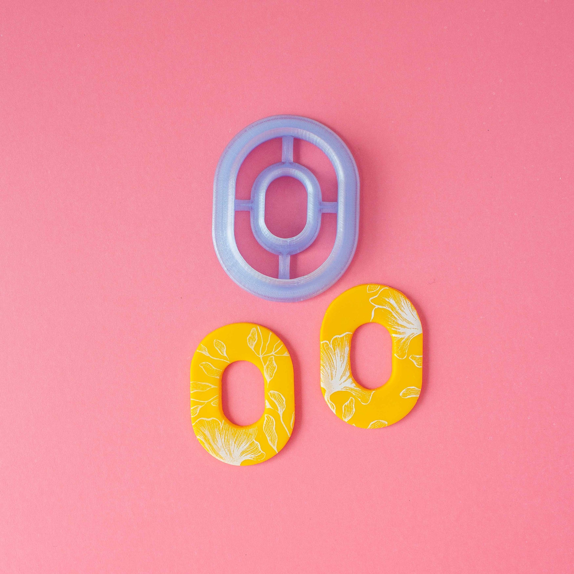 Double oval polymer clay cutter and a set of oval earrings in a pink background.
