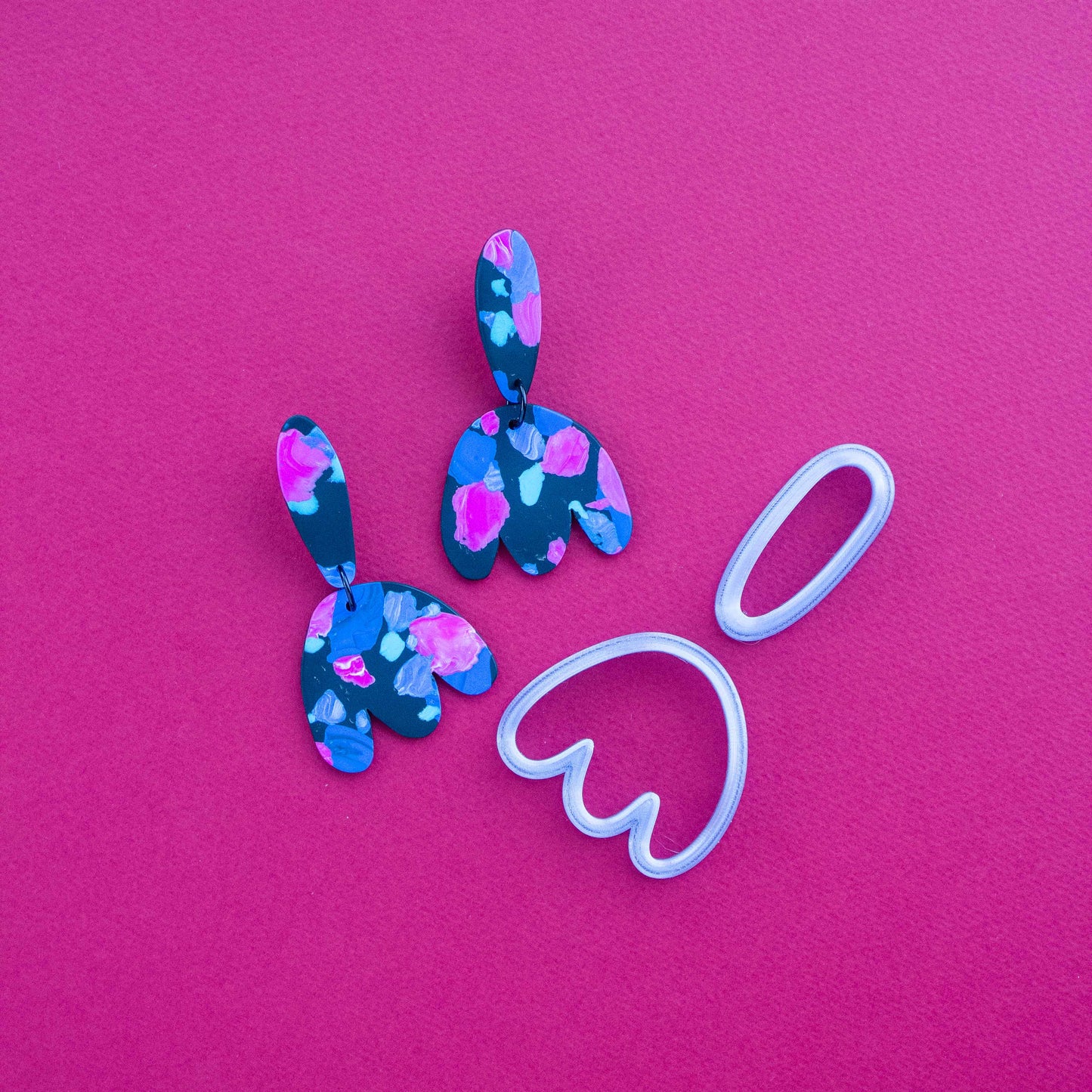 2 earring sets and one abstract flower polymer cutter on a pink background.