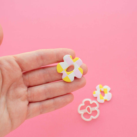 Small polymer clay flower earring in a hand and a cutter in a oink background