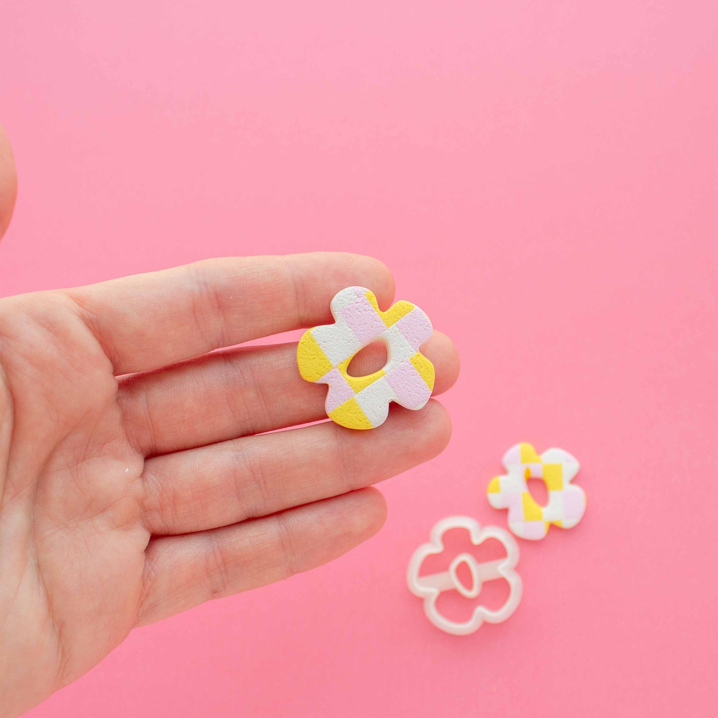 Small polymer clay flower earring in a hand and a cutter in a oink background