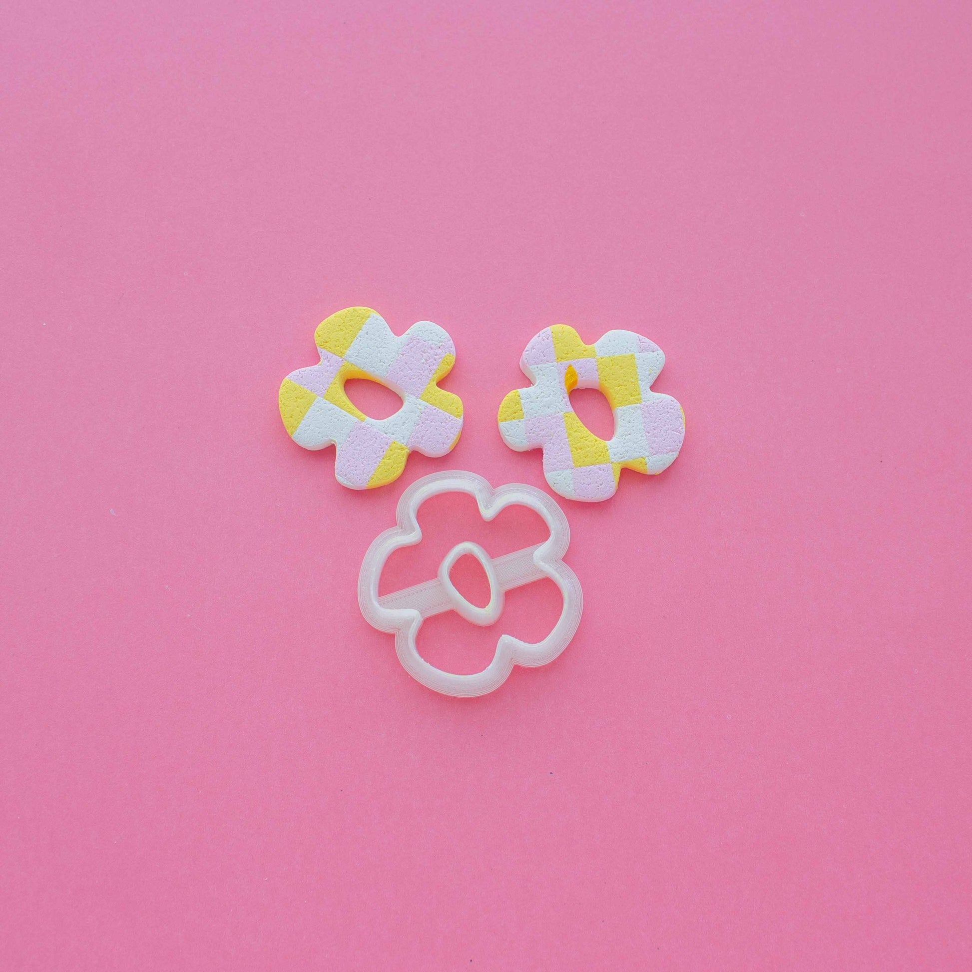 Two small flower abstract earrings and a clay cutter on a  pink background