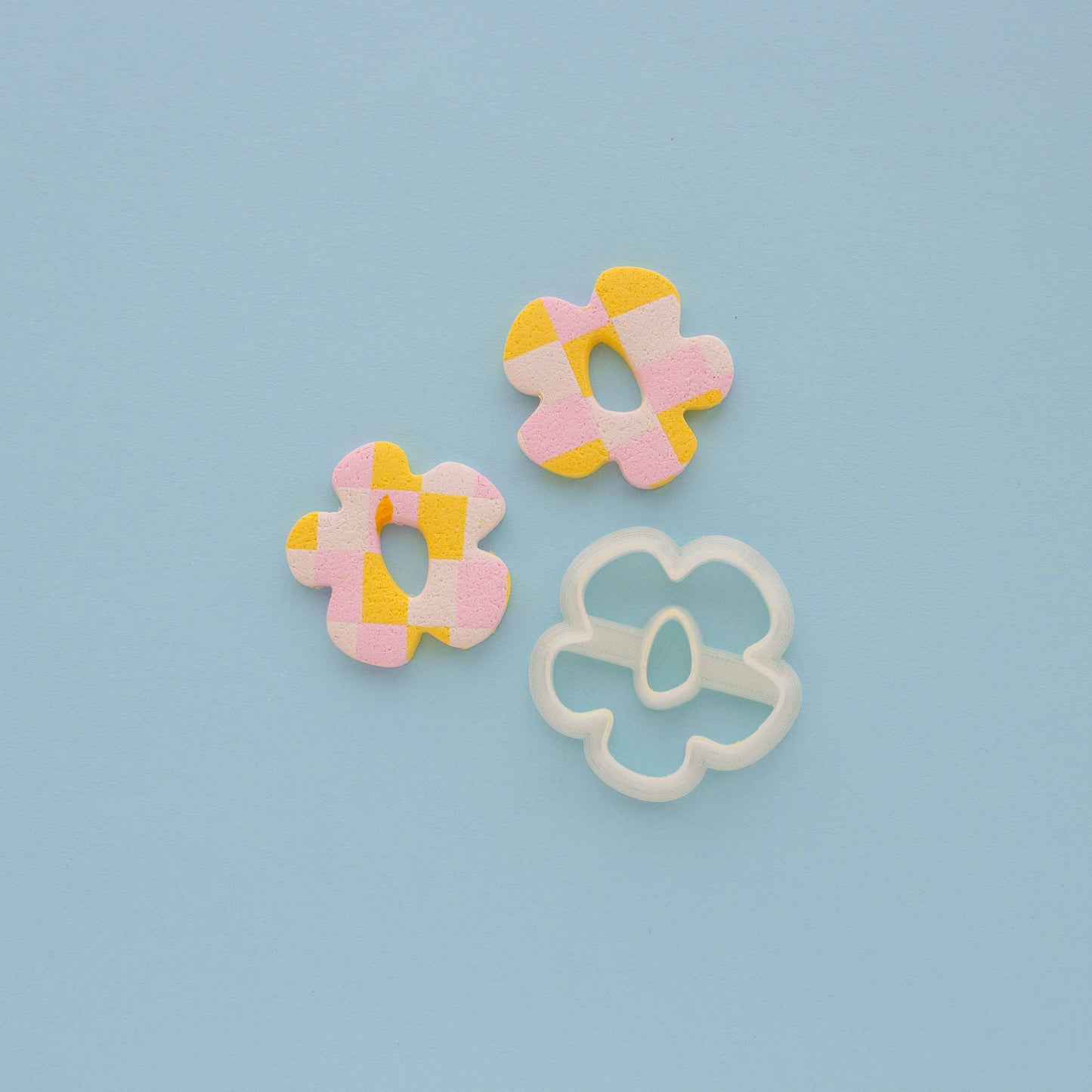 Two small flower abstract earrings and a clay cutter on a light blue background