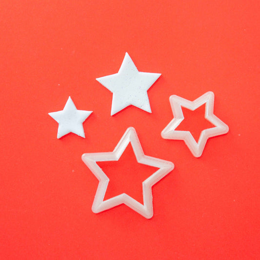2 star shape cutters for clay and 2 polymer clay stars of the same shape on a red background