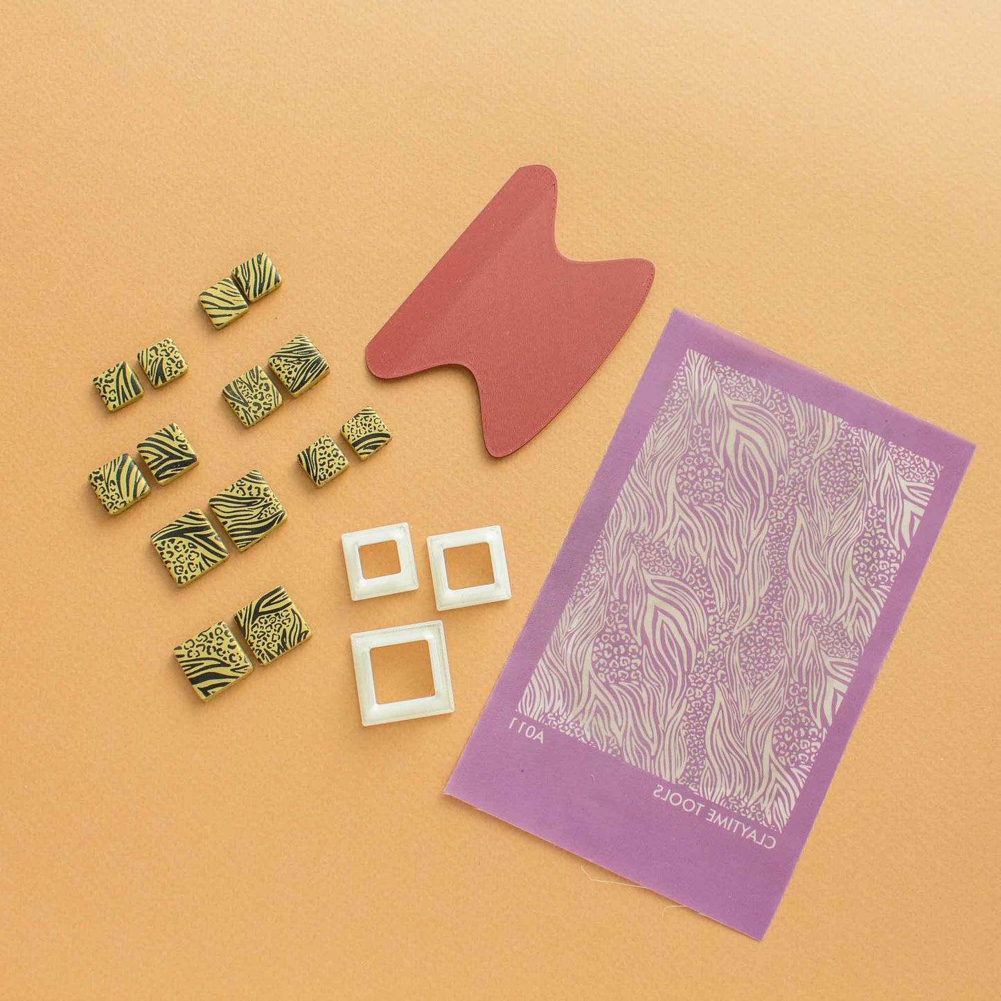 upped view of 1 Animal pattern small silkscreen, some square animal printed polymer clay shapes, 3 square cutters for clay and one squeegee on a light brown background