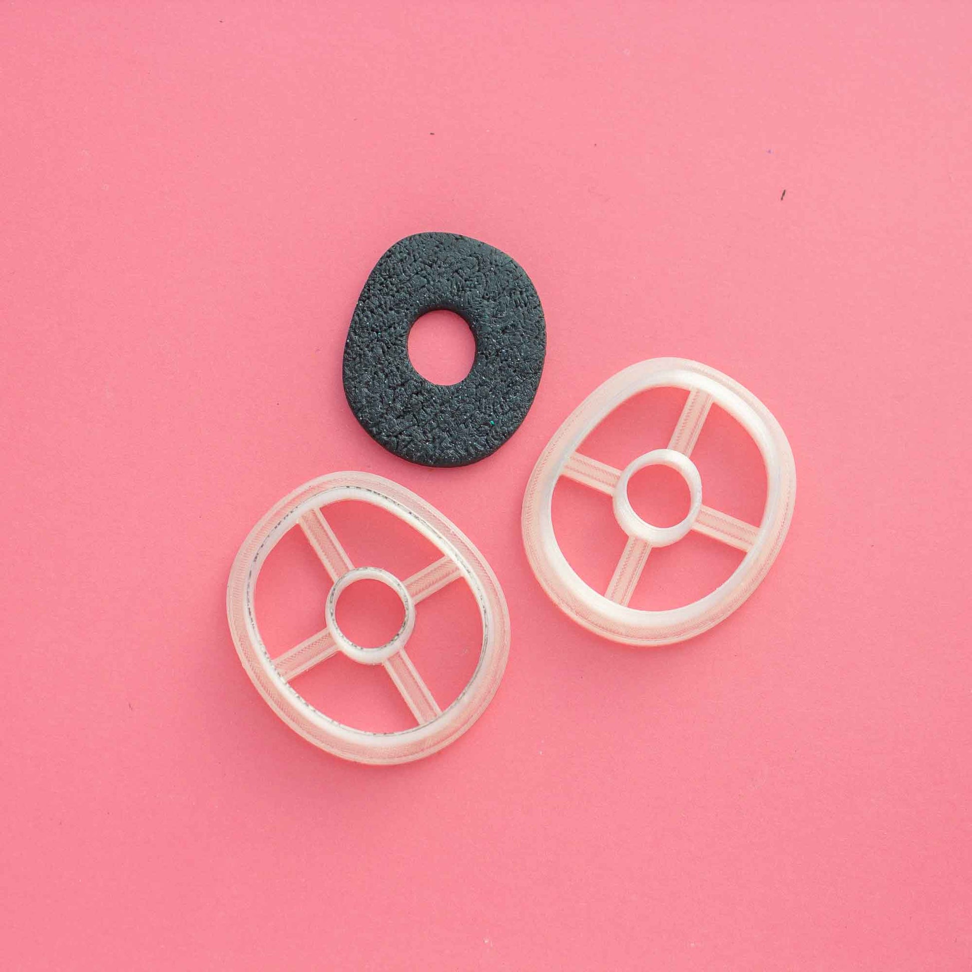 2 mirrored organic circle cutters for clay on a pink background next to a black same shape polymer clay piece