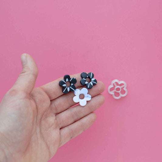 Small daisy flower cutter and three daisy polymer clay earrings on a hand 