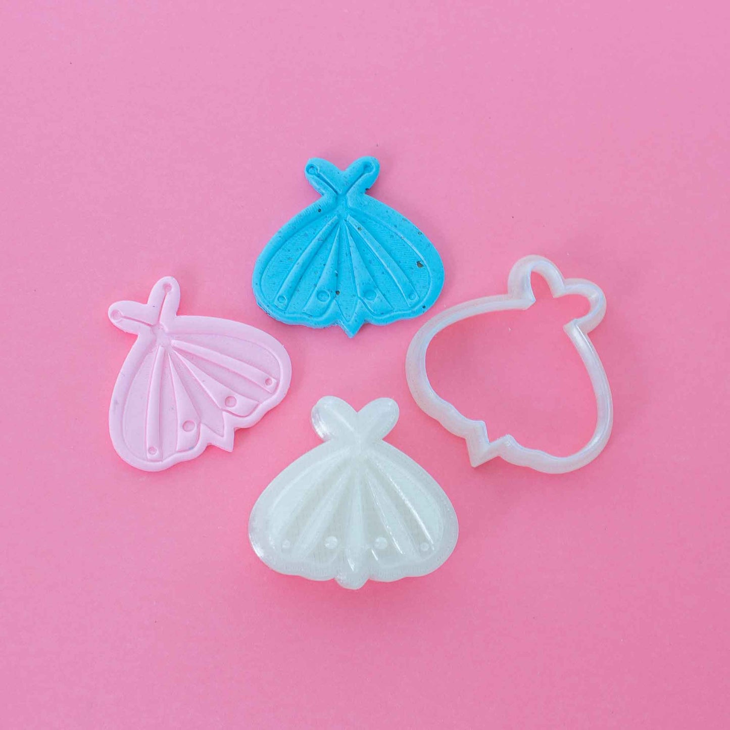 Butterfly stamp and cutter for polymer clay next to 2 colorful clay shapes on a pink background