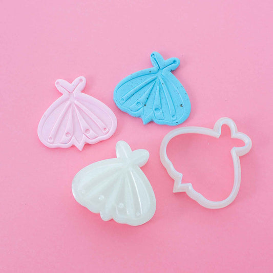 Butterfly stamp and cutter for polymer clay next to 2 colorful clay shapes on a dusty pink background
