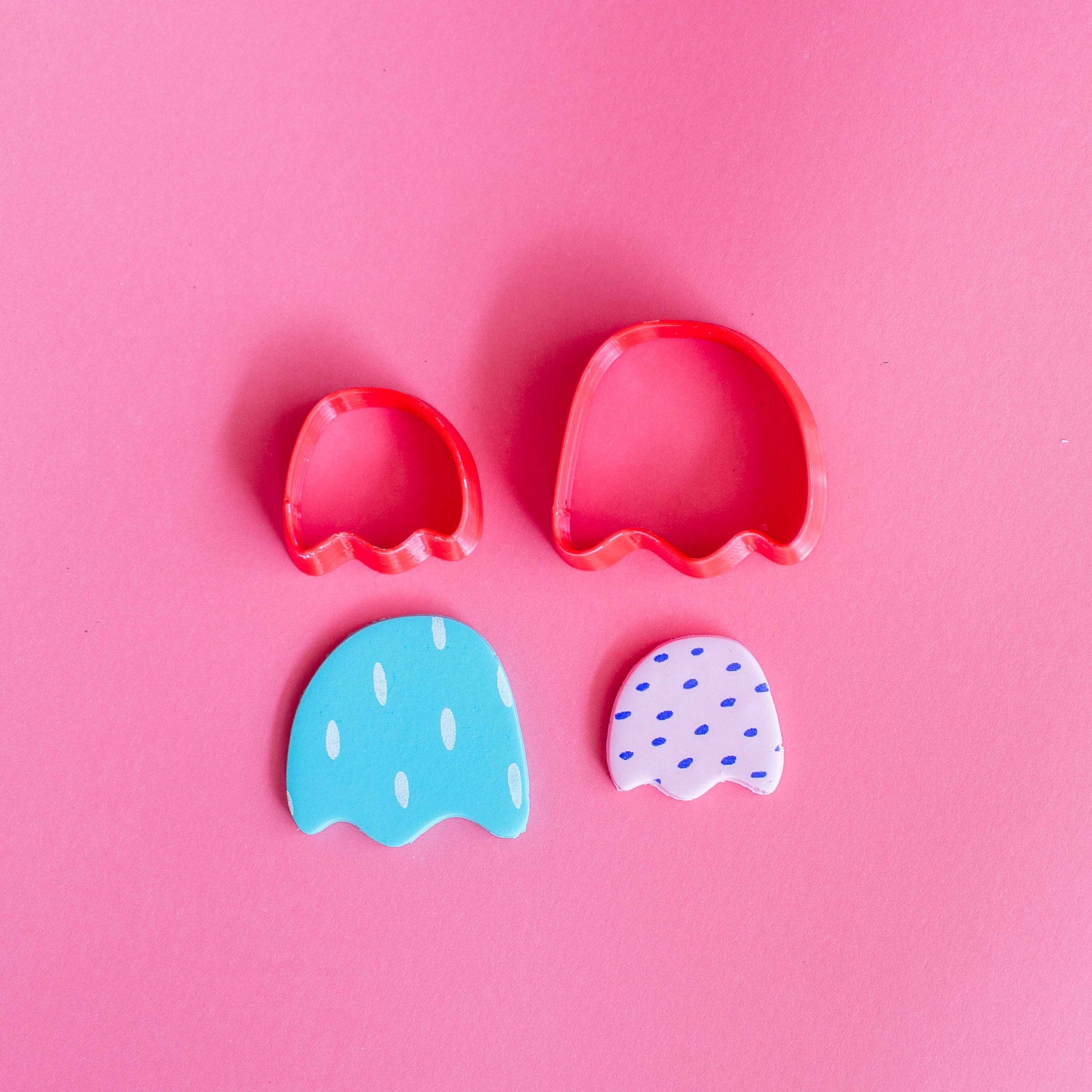 Small and big tulip polymer clay cutters together with two finished pieces of tulip polymer clay earrings on a pink background.
