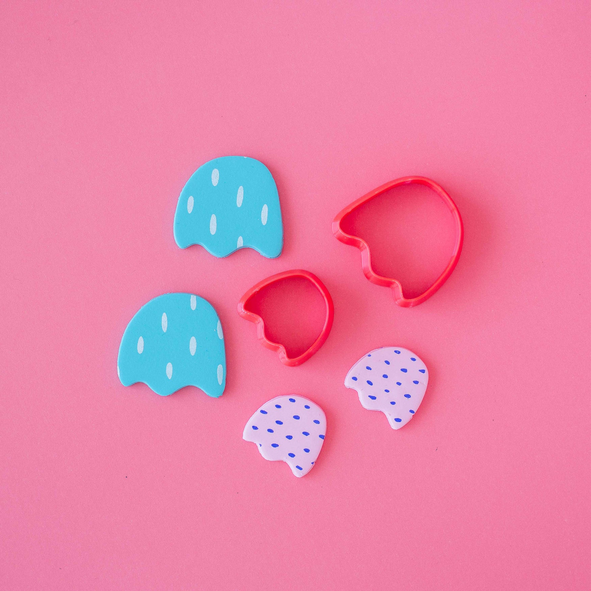 Small and big tulip polymer clay cutters surrounded by four finished pieces of tulip polymer clay earrings on a pink background.