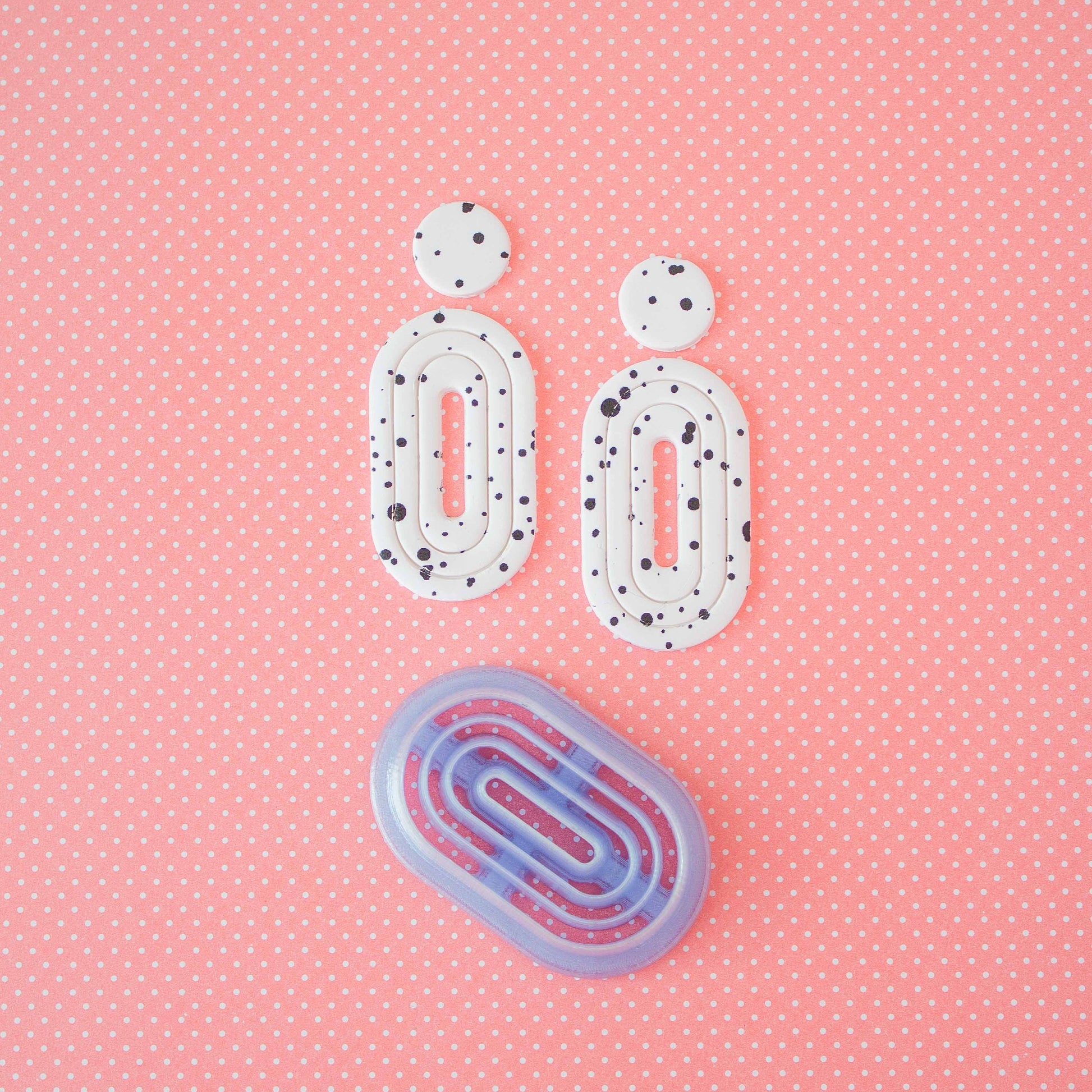 Donut cutter and 2 donut polymer clay earrings on a pink background.