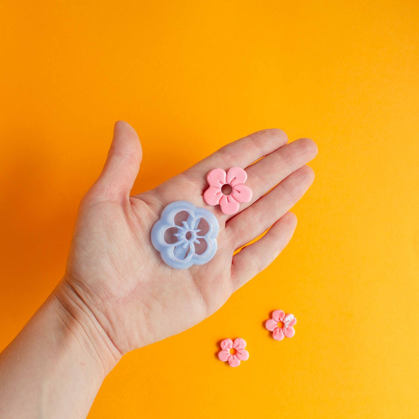 FLower shaped cutter and polymer clay flower displayed on a hand, and two smaller sized clay flowers