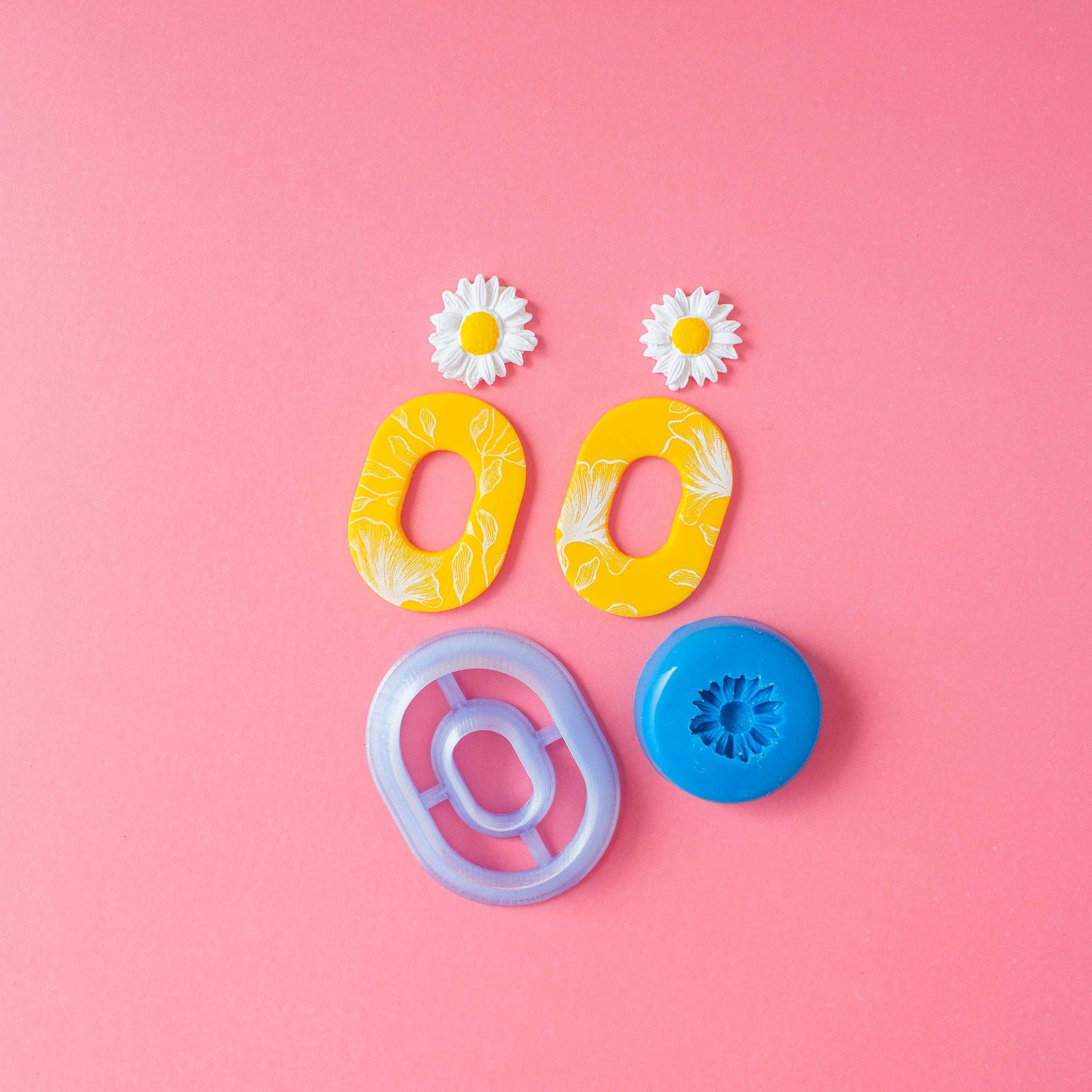 Double oval polymer clay cutter, a daisy silicon mold and a set of oval earrings in a pink background.